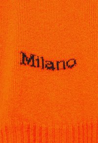 Helle orange Strickjacke mit geripptem Saum, mit schwarzem "Milano" Textlogo. Der Stoff scheint weich und gestrickt zu sein und zeigt eine einheitliche Textur.