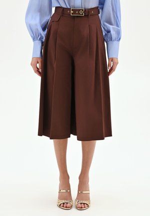 Culottes marron taille haute à jambes larges avec plis devant, associées à un chemisier bleu à manches bouffantes et des sandales dorées à brides.