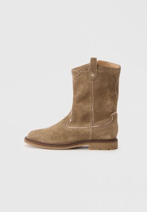 Bota de tornozelo em camurça castanha com bico arredondado, costura decorativa, alça para puxar e sola de borracha. Branding subtil na lateral.