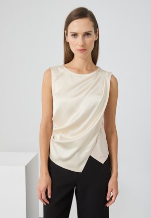 Satin kremfarget ermeløs topp med drapering, asymmetrisk kant og en jevn tekstur, kombinert med svarte bukser.