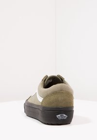 Baskets Vans vert olive avec une bande blanche et une semelle noire, vues de dos sur une surface blanche avec un fond blanc.