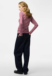 Rot-weiß gestreiftes Langarmshirt kombiniert mit weiten dunkelblauen Jeans mit Taschen und lockerem Sitz. Glatte Stofftextur.