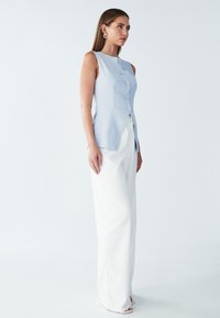 Hele sinine ilma varrukateta tops, millel on ees nupud, koos valgete laia jala pükstega, mis näitavad sujuvat tekstuuri ja kohandatud lõiget.