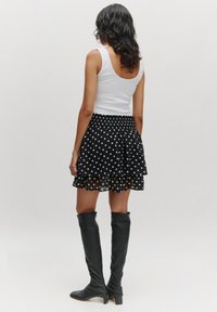Zwarte rok met polkadots, gelaagde ruffles en een smocktail. Gecombineerd met zwarte leren laarzen tot de knie en een witte tanktop.