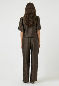 Conjunto marrón de dos piezas con una tela texturizada de patrón en ondas. La parte superior tiene mangas cortas abullonadas, y los pantalones tienen un diseño de pierna recta.