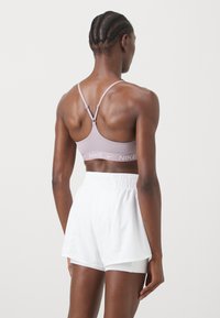 Sujetador deportivo de color púrpura claro con un diseño que ofrece soporte y tirantes ajustables, combinado con pantalones cortos deportivos blancos con cintura elástica.