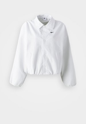 Weiße kurze Jacke mit Kragen, elastischem Bund und langen Puffärmeln. Auf der linken Brust befindet sich ein schwarzes Nike-Logo. Glatte Stofftextur.