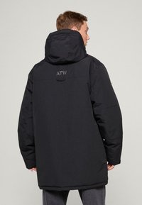 Čierna dlhá prešívaná bunda s kapucňou, s hladkou textúrou a jemným prešívaním. Na chrbte je napísané "ATW" sivým písmom.