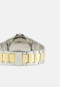 Silver- och guldmetallklocka med ett tvåfärgat armband. Armbandet har växelvis blanka silver- och guld-länkar och ett spänne som syns tydligt.