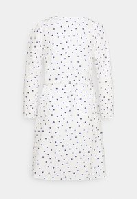 Robe blanche avec des pois bleus, manches longues, une ceinture à la taille, et une coupe droite, avec une texture de tissu lisse.