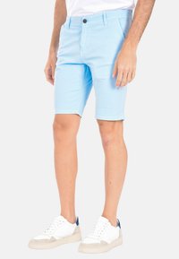 Pantaloni corti azzurri chiari in cotone, con chiusura a bottone, tasche laterali e vestibilità comoda, abbinati a sneakers bianche.