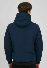 Navy blue puffer jacket with a hood and ribbed cuffs. Smooth, insulated fabric with a slightly shiny finish, designed for warmth.