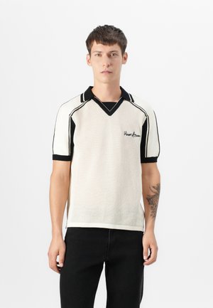 Gestricktes kurzärmeliges Poloshirt in Creme mit schwarzen Akzenten. Verfügt über einen V-Ausschnitt und ein eingesticktes Logo. Strukturierter Stoff und figurbetontes Design.