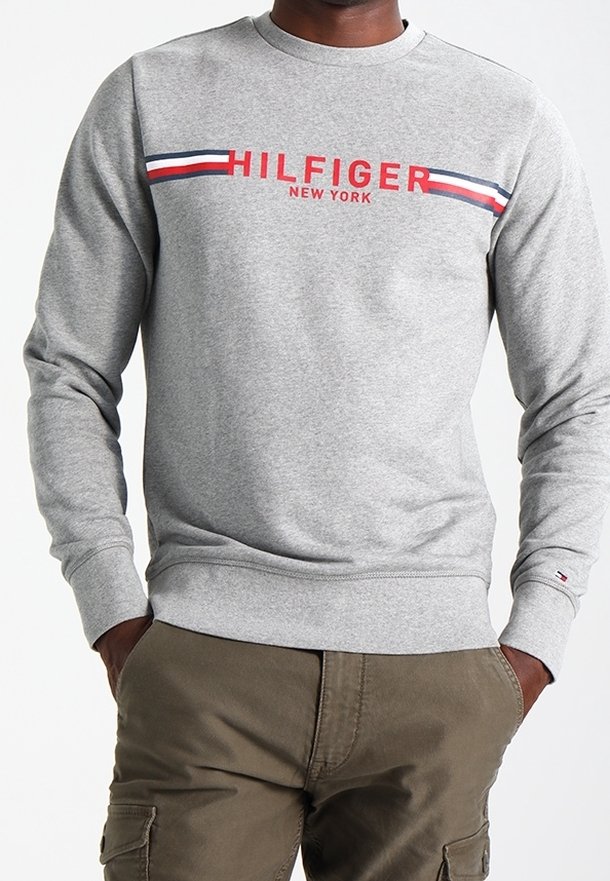 Grauer Sweatshirt mit Rundhalsausschnitt, mit rotem "HILFIGER"-Schriftzug und horizontalen roten, weißen und blauen Streifen über der Brust. Weicher Stoff.