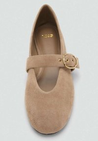 Beżowy zamszowy płaski but typu Mary Jane z zaokrąglonym czubkiem i regulowanym paskiem z złotą klamrą na górze.