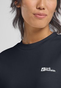 Maglietta nera a maniche corte con scollatura a girocollo, con logo bianco "Jack Wolfskin" e dettaglio di impronta di zampa sul lato sinistro del petto.