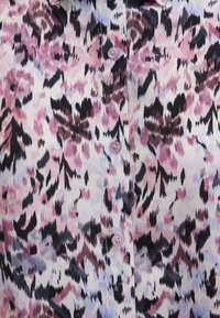 Hemd mit Knopfleiste, das ein florales Muster in Rosa, Lila, Schwarz und Hellblau auf einem cremefarbenen Hintergrund zeigt. Weicher Stoff mit rosa Knöpfen.