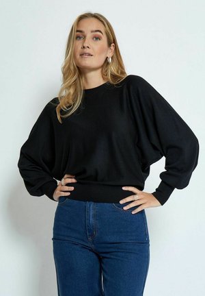 Schwarzer, übergroßer Pullover mit Fledermausärmeln, geripptem Saum und weicher Textur, kombiniert mit hochgeschnittenen blauen Jeans. Einfaches, minimales Design.