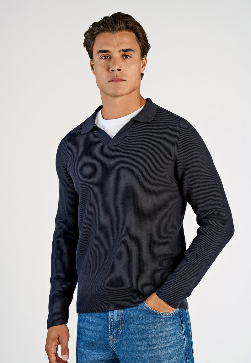 Marineblauer Rippstrickpullover mit V-Ausschnitt und Kragen, mit langen Ärmeln und strukturiertem Stoff. Kombiniert mit blauen Denim-Jeans.