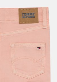 Różowa denimowa tkanina z widocznym detalem kieszeni, beżowa skórzana metka z wytłoczonym napisem "TOMMY HILFIGER" oraz mały akcent z logo.