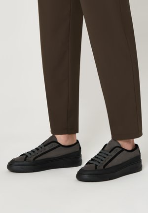 Sneaker nere e grigie con una parte superiore texture, suole nere piatte e lacci grigi, caratterizzati da un design slanciato e colletto imbottito.