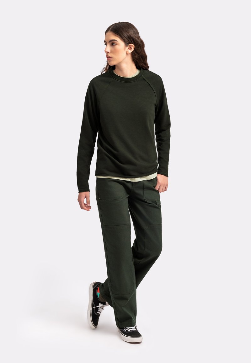 Camicia a maniche lunghe verde scuro con maniche raglan abbinata a pantaloni cargo verde scuro con più tasche e una vestibilità rilassata. Sneakers nere.