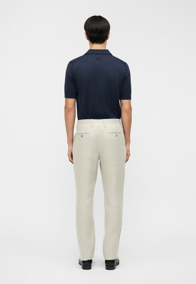 Polo azul marino de manga corta, combinado con pantalones de lino beige y zapatos negros. Cuenta con un cuello estándar y un logo discreto en la parte trasera.