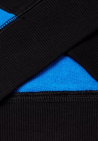 Primo piano di un tessuto nero a righe sovrapposto a un tessuto blu brillante con texture, con cuciture visibili lungo i bordi.