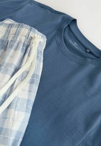 Blå t-shirt med rund hals kombineret med hvide og lyseblå ternede bukser med snøre på en lys baggrund.