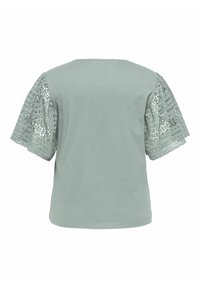 T-shirt verde chiaro con maniche corte a fantasia di pizzo. Tessuto morbido e texture, con scollatura rotonda e vestibilità ampia.