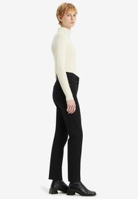 Suéter de cuello alto acanalado en crema combinado con pantalones negros ajustados, llevado con botas de tobillo de tacón negro. Silueta sencilla y ajustada.