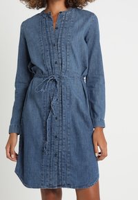 Jeansklänning med långa ärmar, knapplåst fram, plisserade detaljer och knytmidja. Färgen är mörkblå med en slät textur.