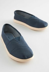 Baskets slip-on en toile bleu marine avec un tissu texturé, couture supérieure en forme de V et semelle en caoutchouc crème. L'intérieur présente un motif rayé.