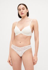 Soutien-gorge blanc en tissu lisse avec bretelles réglables, accompagné d'un string blanc assorti avec une bordure en dentelle au niveau de la taille.