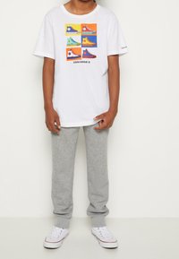 Hvid bomulds T-shirt med farverig sneakers grafik; parret med grå sweatpants og hvide sneakers. Turtleneck, afslappet pasform.