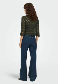 Haut crochet vert foncé à manches trois-quarts avec un ourlet en scallop, associé à un jean en denim à taille haute et à pattes larges. Motif ajouré notable.