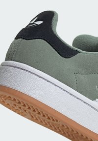 Zelené semišové tenisky s čiernym akcentom na päte, bielou gumovou medzipodrážkou a gumovou podošvou s textúrovaným vzorom.