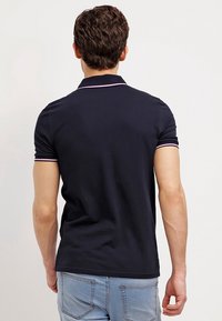 Camiseta polo azul marino de manga corta, con un cuello clásico y acentos a rayas rosas contrastantes a lo largo del cuello y las mangas.