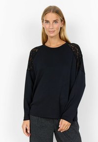 Black long-sleeve top with lace accents on shoulders. Relaxed fit, soft fabric, crew neck. Paired with gray textured pants.