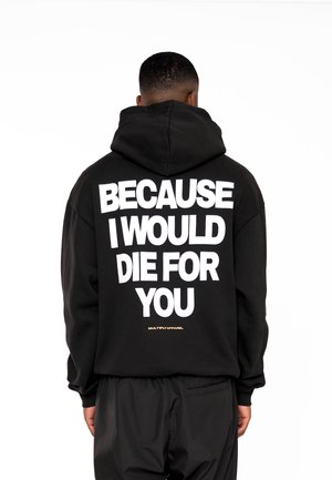 Personne vue de dos portant un sweat à capuche noir avec un texte blanc disant « BECAUSE I WOULD DIE FOR YOU » et un pantalon noir.