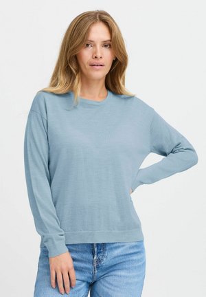 Pull long à manches longues de couleur bleu clair en tissu doux, avec un col rond et une coupe décontractée. Porté avec un jean en denim classique.