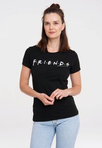 Black cotton t-shirt with short sleeves, featuring "F.R.I.E.N.D.S." in colorful letters across the chest. Fitted design. Light blue jeans worn.