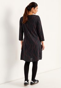 Svart klänning med röd vågmönster, trekvartsärmar, knälång, kombinerad med svarta leggings och sportskor. Slät textur och avslappnad passform.