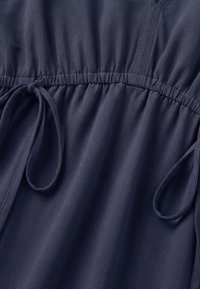 Section de vêtement bleu foncé avec taille élastique froncée et liens étroits en tissu de chaque côté formant des boucles.