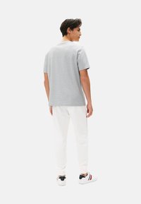 Camiseta de algodón gris con mangas cortas, combinada con joggers blancos y zapatillas con detalles en negro, vista desde la parte trasera. Diseño simple.