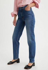Vaqueros de mezclilla azules de tiro alto con un diseño de pierna recta y un estilo clásico de cinco bolsillos. El material parece de peso medio con un ligero desvanecimiento.