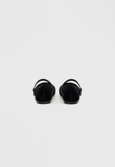 Ballerines noires en suède avec une forme arrondie, une sangle arrière et des détails en métal argenté. Texture lisse avec un design minimaliste.