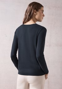 Czarny sweter z długim rękawem i okrągłym dekoltem, o gładkiej fakturze i prostym wzornictwie, zestawiony z kremowymi spodniami.