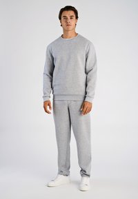 Grijze trui en joggingbroek outfit gemaakt van een zachte katoenmix stof. Voorzien van een klassieke ronde hals en elastische manchetten. Draagt witte sneakers.