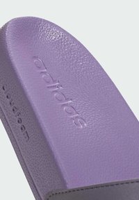 Fioletowe klapki Adidas z teksturowaną powierzchnią, z wytłoczonym logo. Projekt zawiera wytłaczaną wkładkę dla komfortu.